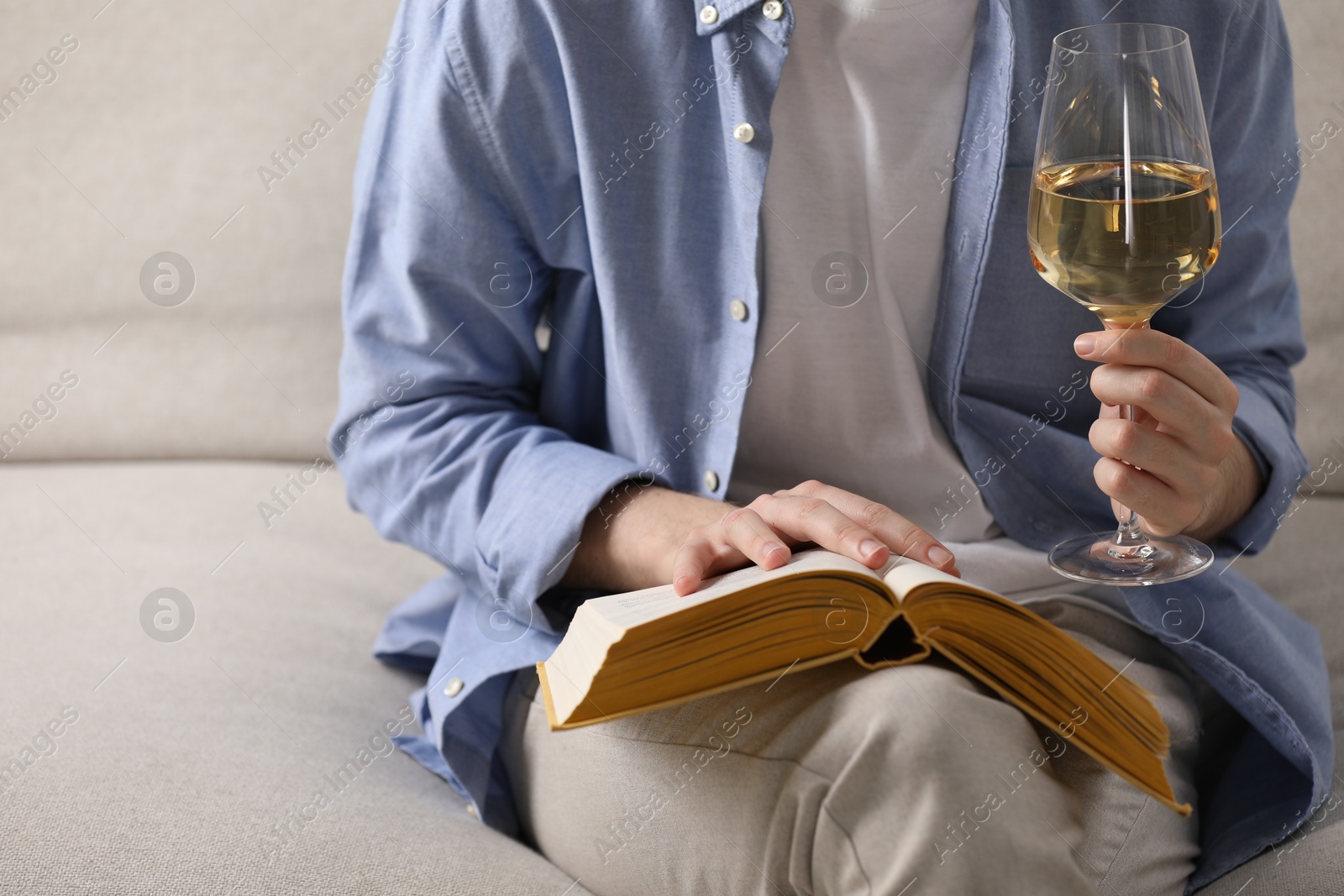 Woman with glass of wine reading book on sofa at home, closeup Photo of Woman with glass of wine reading book on sofa at home, closeup