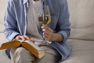 Photo of Woman with glass of wine reading book on sofa at home, closeup