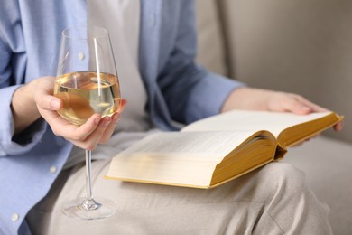 Photo of Woman with glass of wine reading book on sofa at home, closeup