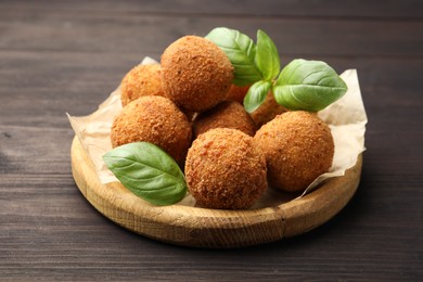 Photo of Delicious fried croquette balls with basil on wooden table, closeup