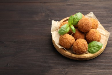 Photo of Delicious fried croquette balls with basil on wooden table. Space for text