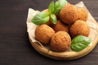 Photo of Delicious fried croquette balls with basil on wooden table, closeup