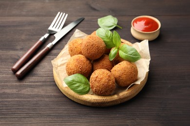 Photo of Delicious fried croquette balls with basil on wooden table, closeup