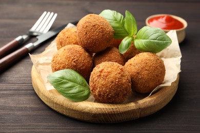 Photo of Delicious fried croquette balls with basil on wooden table, closeup