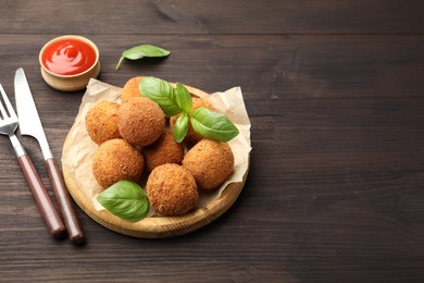 Photo of Delicious fried croquette balls with basil, cutlery and ketchup on wooden table. Space for text