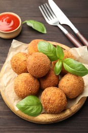 Photo of Delicious fried croquette balls with basil on wooden table, closeup