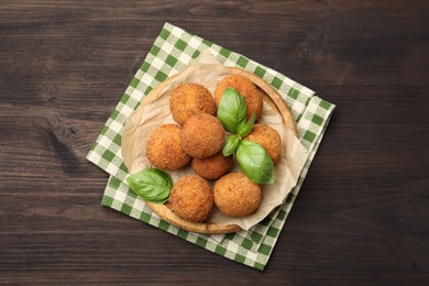 Photo of Delicious fried croquette balls with basil on wooden table, top view