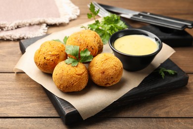 Photo of Delicious fried croquette balls with parsley and sauce on wooden table, closeup