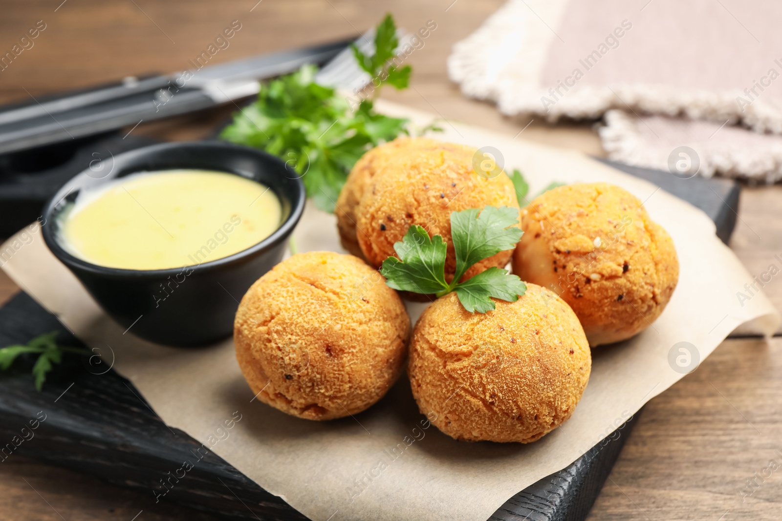 Photo of Delicious fried croquette balls with parsley and sauce on wooden table, closeup