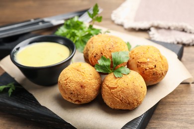 Photo of Delicious fried croquette balls with parsley and sauce on wooden table, closeup