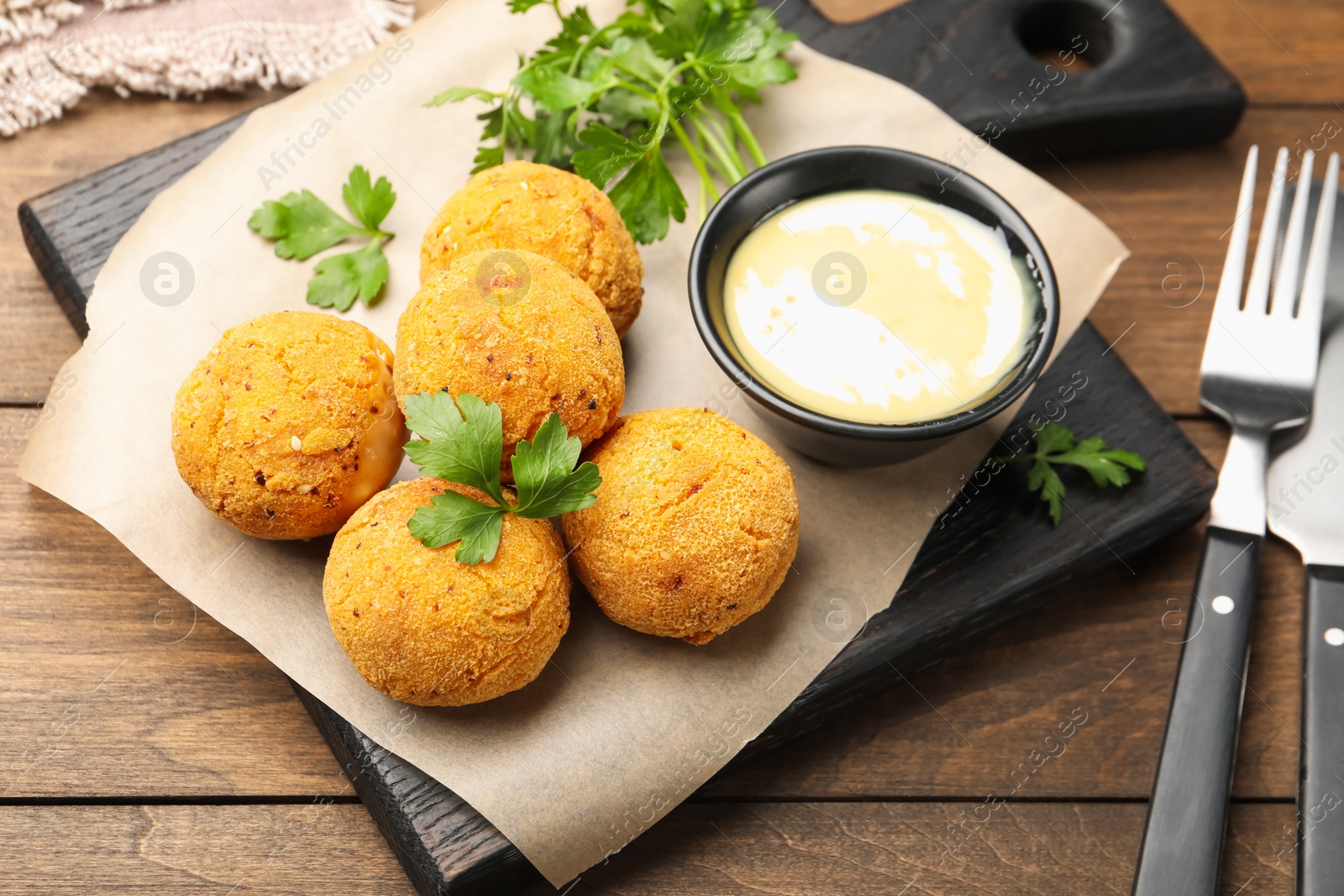 Photo of Delicious fried croquette balls with parsley and sauce on wooden table, closeup