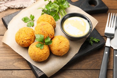 Photo of Delicious fried croquette balls with parsley and sauce on wooden table, closeup