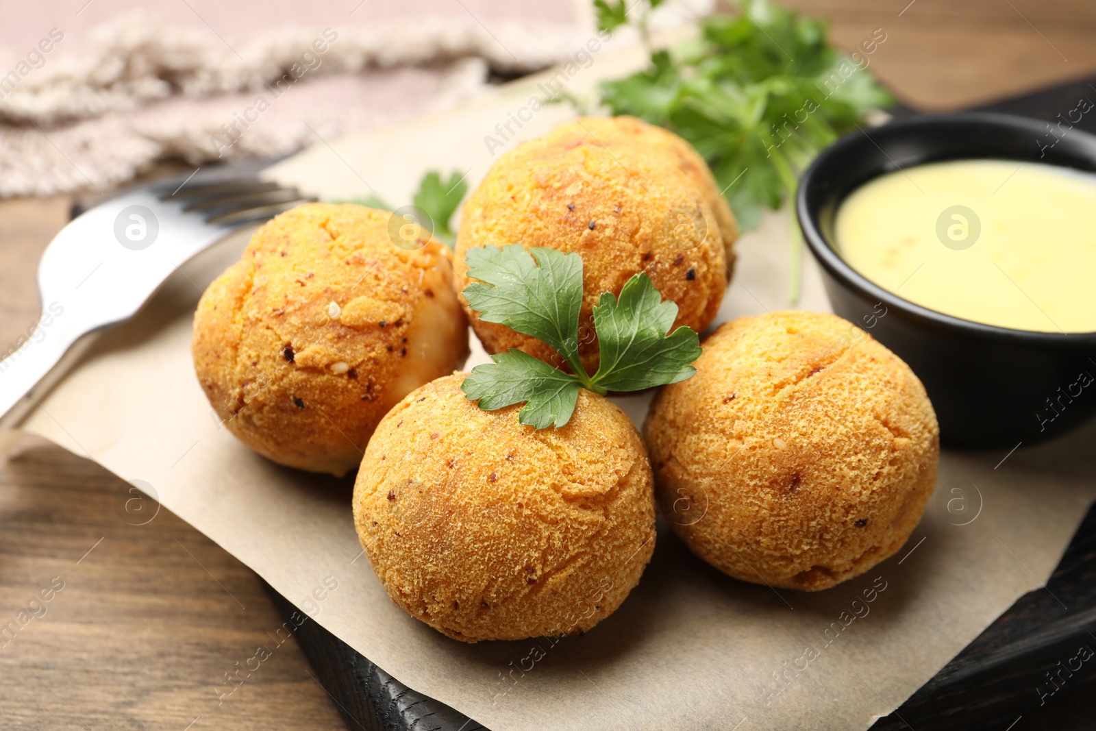 Photo of Delicious fried croquette balls with parsley and sauce on wooden table, closeup