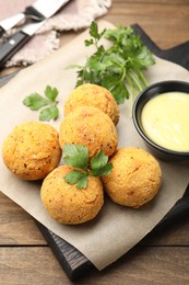 Photo of Delicious fried croquette balls with parsley and sauce on wooden table