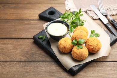 Photo of Delicious fried croquette balls with parsley and sauce on wooden table, closeup