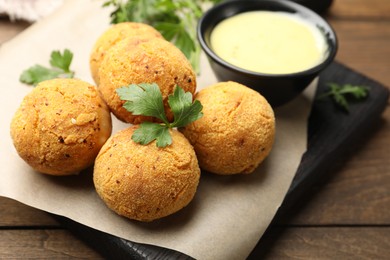 Photo of Delicious fried croquette balls with parsley and sauce on wooden table, closeup