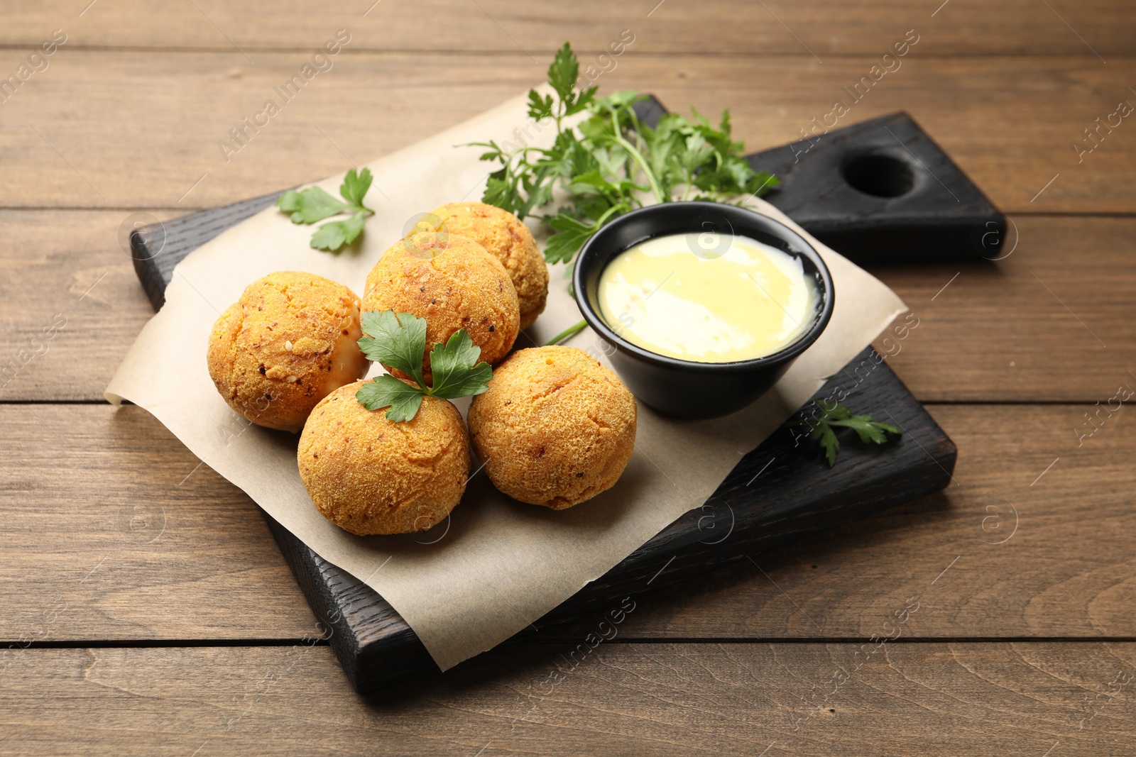 Photo of Delicious fried croquette balls with parsley and sauce on wooden table, closeup