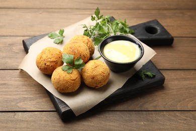 Photo of Delicious fried croquette balls with parsley and sauce on wooden table, closeup