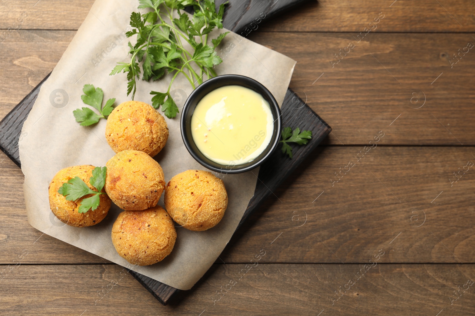 Photo of Delicious fried croquette balls with parsley and sauce on wooden table, top view. Space for text