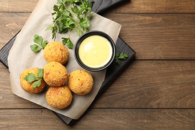 Photo of Delicious fried croquette balls with parsley and sauce on wooden table, top view. Space for text