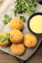 Photo of Delicious fried croquette balls with parsley and sauce on wooden table, top view