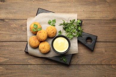 Photo of Delicious fried croquette balls with parsley and sauce on wooden table, top view