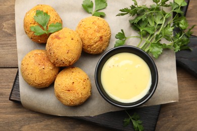 Photo of Delicious fried croquette balls with parsley and sauce on wooden table, top view