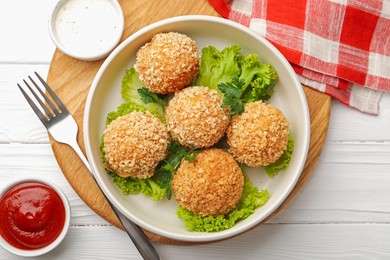 Photo of Delicious fried croquette balls with parsley, lettuce and sauces on white wooden table, flat lay