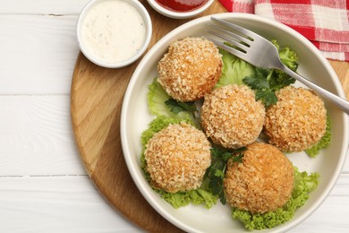 Photo of Delicious fried croquette balls with parsley, lettuce and sauces on white wooden table, top view