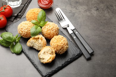 Photo of Delicious fried croquette balls with basil on grey textured table, closeup