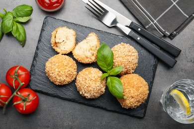 Photo of Delicious fried croquette balls with basil served on grey textured table, flat lay