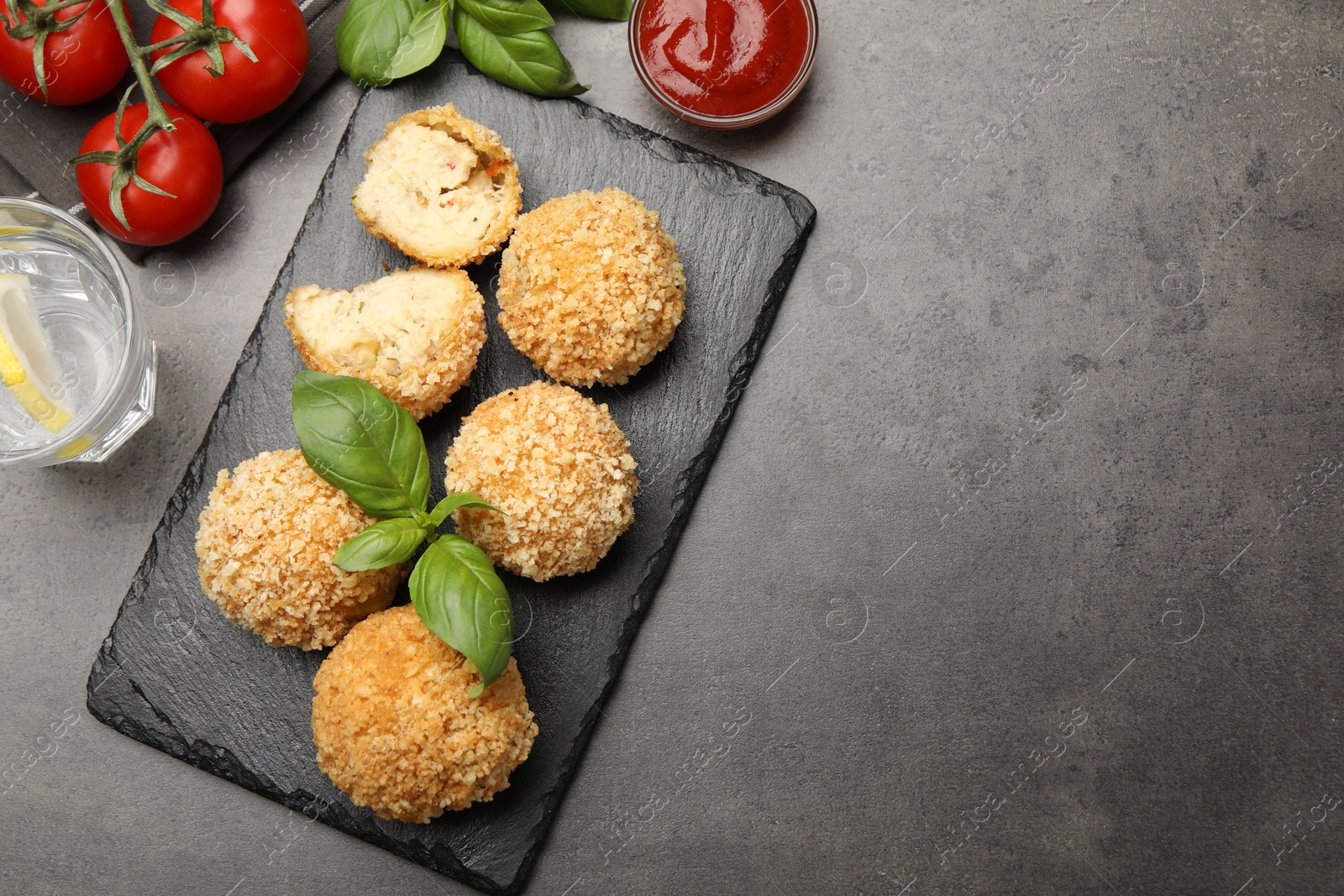 Delicious fried croquette balls with basil, tomato, water and ketchup on grey textured table, flat lay. Space for text Photo of Delicious fried croquette balls with basil, tomato, water and ketchup on grey textured table, flat lay. Space for text