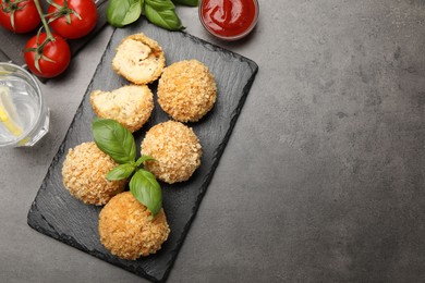 Photo of Delicious fried croquette balls with basil, tomato, water and ketchup on grey textured table, flat lay. Space for text