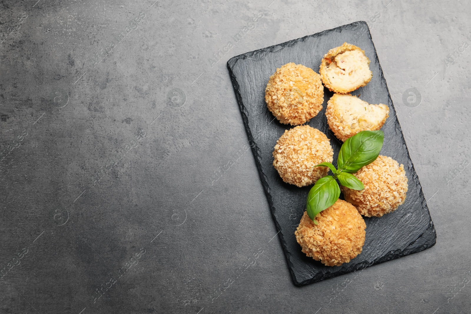 Photo of Delicious fried croquette balls with basil on grey textured table, top view. Space for text