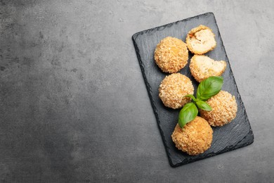 Photo of Delicious fried croquette balls with basil on grey textured table, top view. Space for text