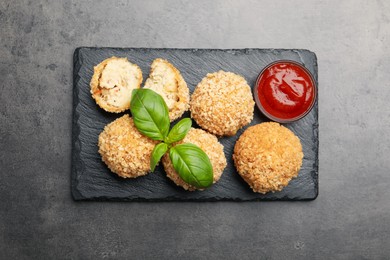 Photo of Delicious fried croquette balls with basil and ketchup on grey textured table, top view