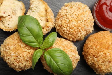 Photo of Delicious fried croquette balls with basil and ketchup on grey textured table, flat lay