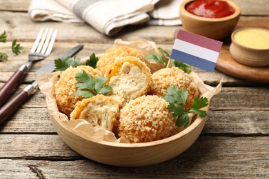 Photo of Delicious fried croquette balls, parsley and small flag of Netherlands on wooden table, closeup