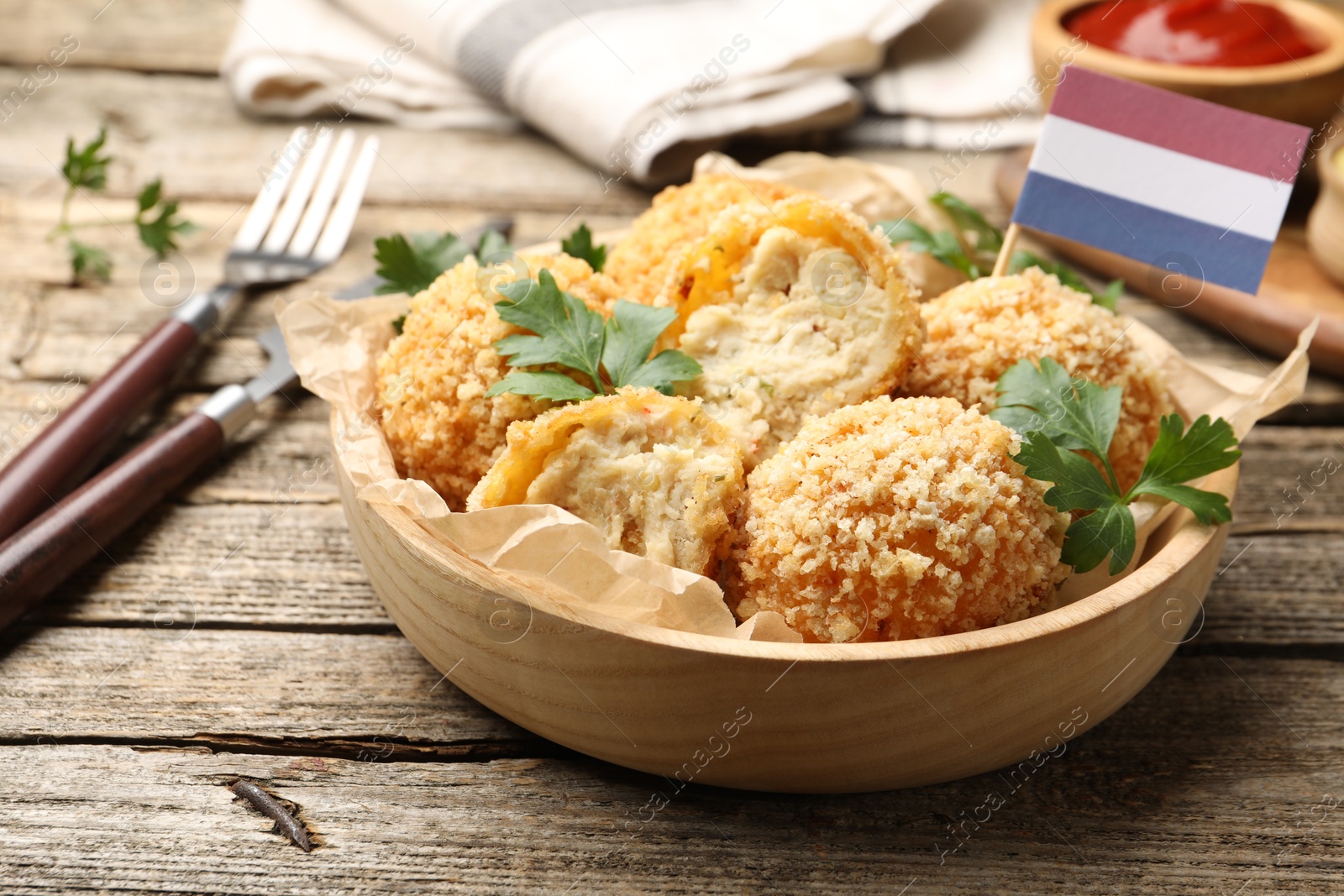 Photo of Delicious fried croquette balls, parsley and small flag of Netherlands on wooden table, closeup