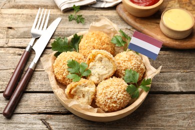 Photo of Delicious fried croquette balls, parsley and small flag of Netherlands on wooden table, closeup