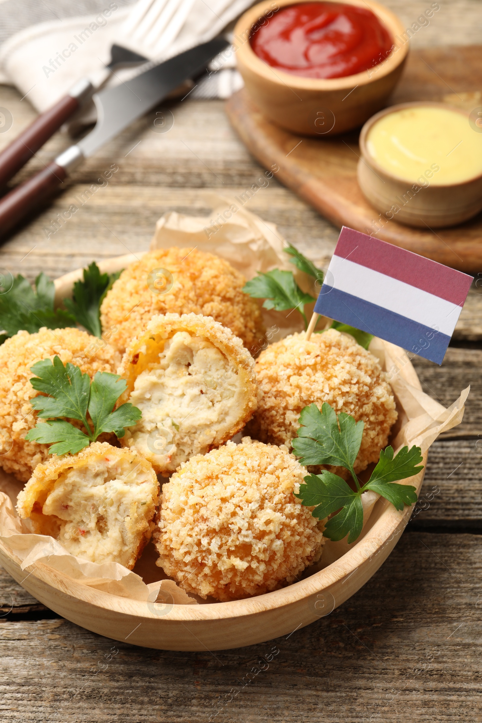 Photo of Delicious fried croquette balls, parsley and small flag of Netherlands on wooden table, closeup