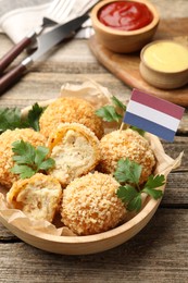 Photo of Delicious fried croquette balls, parsley and small flag of Netherlands on wooden table, closeup