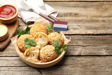 Photo of Delicious fried croquette balls, parsley and small flag of Netherlands on wooden table, closeup. Space for text
