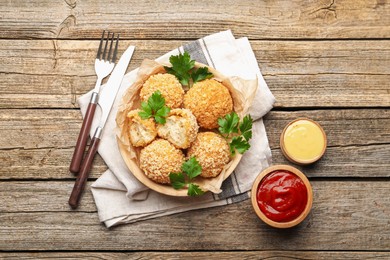 Photo of Delicious fried croquette balls with parsley and sauces served on wooden table, flat lay