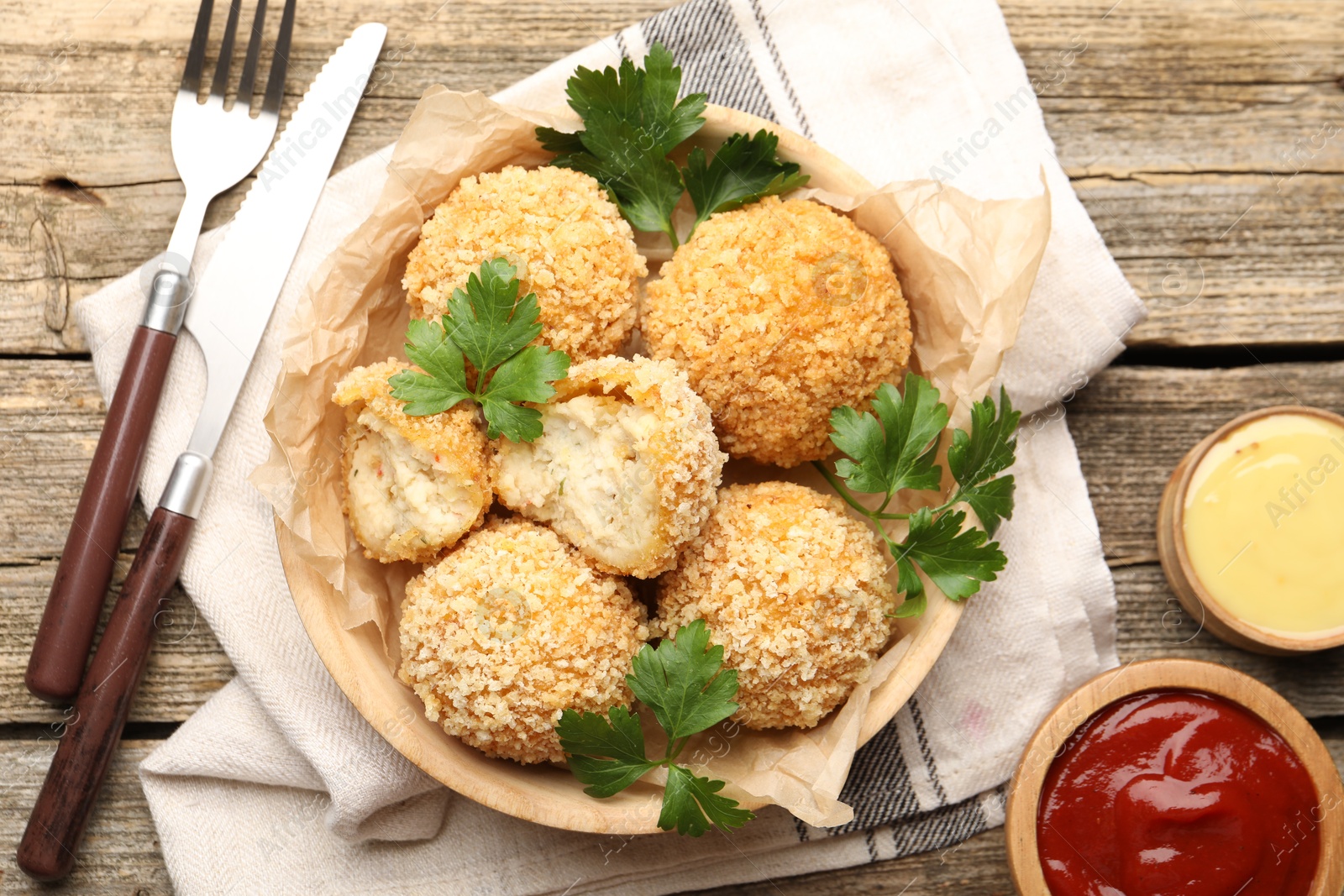 Photo of Delicious fried croquette balls with parsley and sauces served on wooden table, flat lay