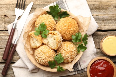 Photo of Delicious fried croquette balls with parsley and sauces served on wooden table, flat lay