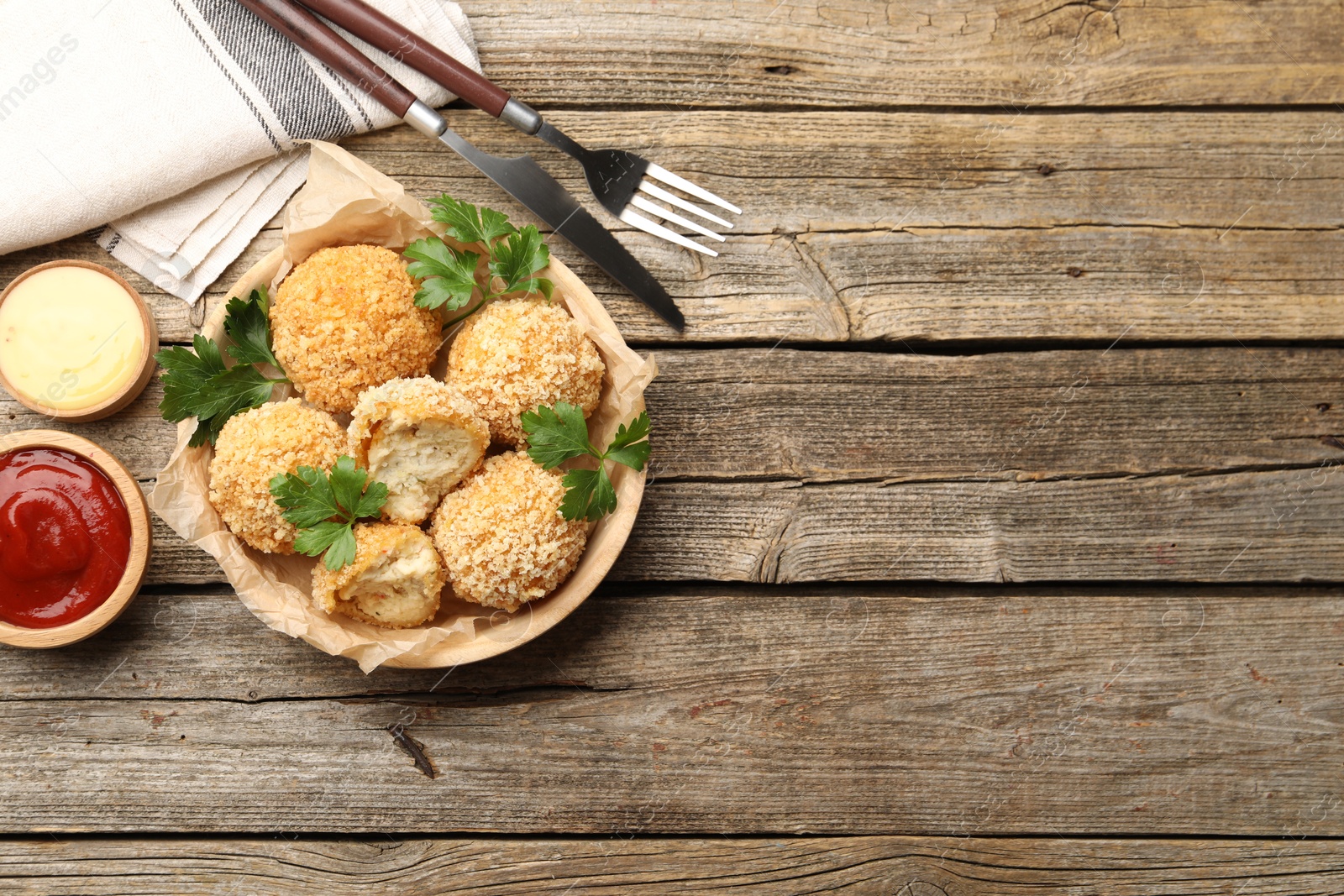 Photo of Delicious fried croquette balls with parsley and sauces served on wooden table, flat lay. Space for text