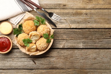 Photo of Delicious fried croquette balls with parsley and sauces served on wooden table, flat lay. Space for text