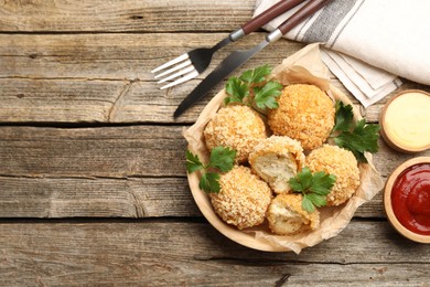 Photo of Delicious fried croquette balls with parsley and sauces served on wooden table, flat lay. Space for text