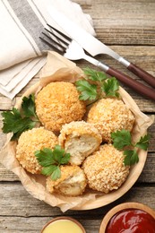 Photo of Delicious fried croquette balls with parsley and sauces served on wooden table, flat lay